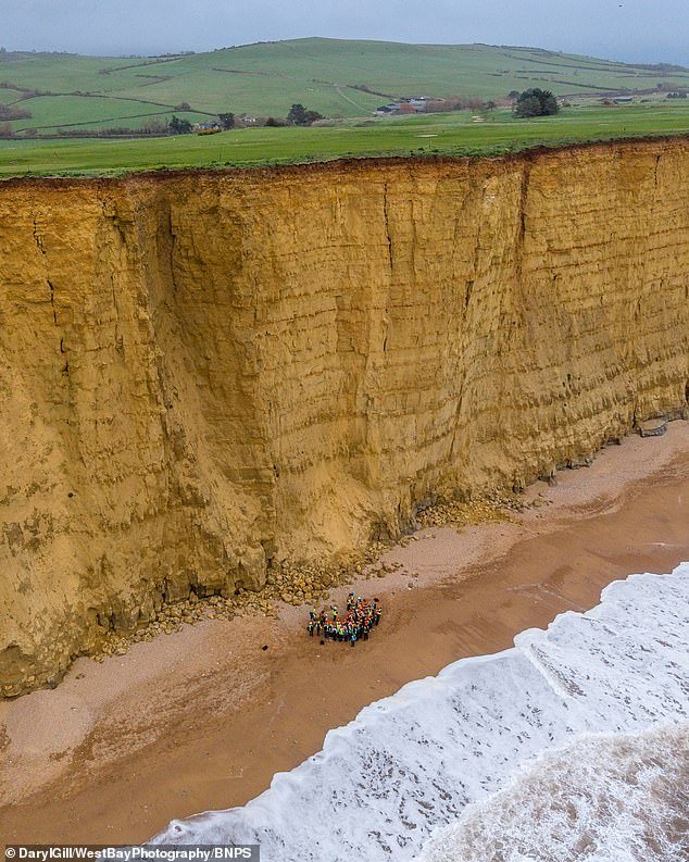 Más de 40 estudiantes de geología están arriesgando sus vidas para pararse debajo de un acantilado de 150 pies que se está desmoronando, ignorando las señales de advertencia de roca que cae.