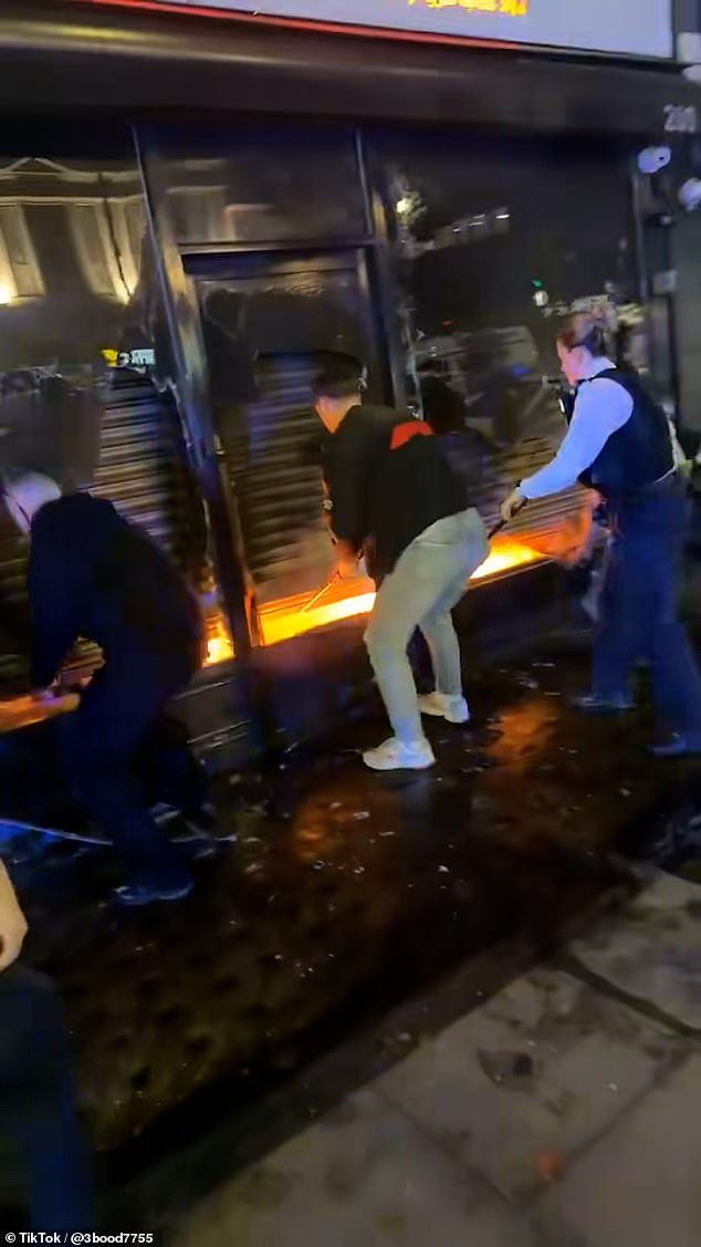 Los héroes transeúntes se abren camino a través de una tienda de comestibles en llamas para salvar a un hombre atrapado dentro mientras rompen las ventanas y abren la contraventana de seguridad.